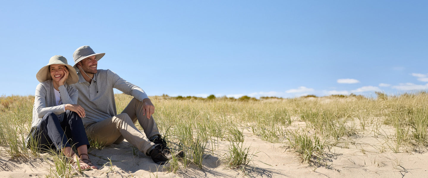 A couple sitting on a beach in sun proof gear.