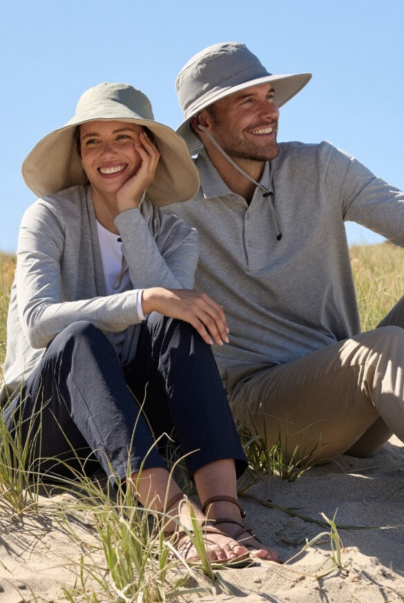 A couple sitting on a beach in sun proof gear.